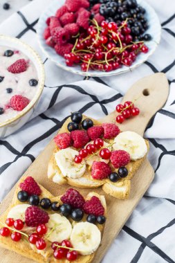Bir tablo ile sağlıklı bir yaz kahvaltı - yulaf ezmesi çilek, kuş üzümü ve ahududu ve fıstık ezmesi, muz ve çeşitli meyveler ile bir sandviç