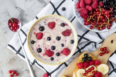 Bir tablo ile sağlıklı bir yaz kahvaltı - yulaf ezmesi çilek, kuş üzümü ve ahududu ve fıstık ezmesi, muz ve çeşitli meyveler ile bir sandviç. Üstten görünüm, düz yatıyordu