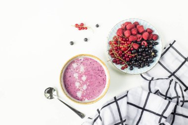 Berry güler yüzlü bir plaka ile ahududu yanındaki bir kapta ve siyah ve kırmızı kuş üzümü siyah-beyaz kareli peçete ile beyaz bir tabloda. Sağlıklı gıda kavramı. Üstten görünüm