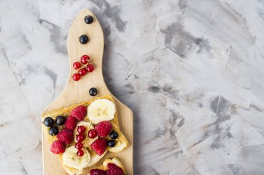 Fıstık ezmesi, muz ve ahududu ve gri bir tablo üzerinde bir ahşap tahta üzerinde kuş üzümü ile Sendvci. Vegan sağlıklı kahvaltı. Üstten görünüm, düz yatıyordu, boşaltmak