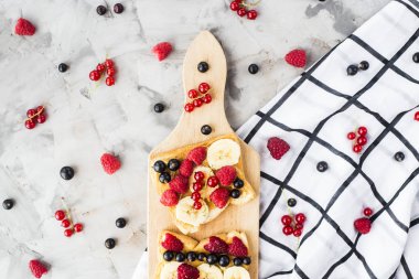 Fıstık ezmesi, muz ve ahududu ve gri bir tablo üzerinde bir ahşap tahta üzerinde kuş üzümü ile Sendvci. Vegan sağlıklı kahvaltı. Üstten görünüm, düz yatıyordu