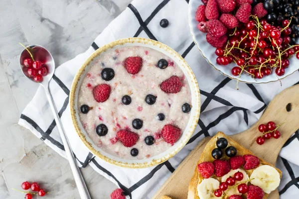 Bir tablo ile sağlıklı bir yaz kahvaltı - yulaf ezmesi çilek, kuş üzümü ve ahududu ve fıstık ezmesi, muz ve çeşitli meyveler ile bir sandviç. Üstten görünüm, düz yatıyordu