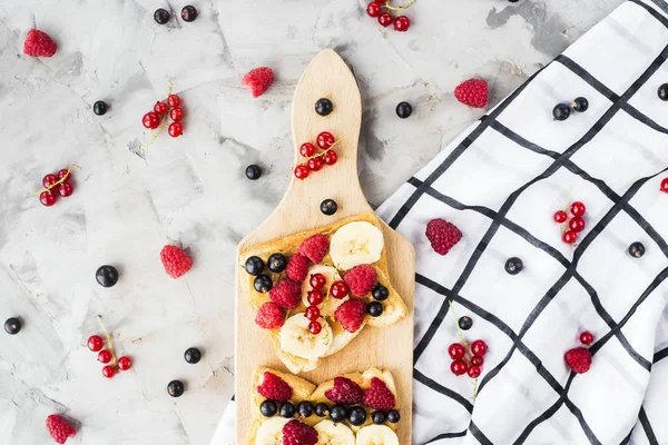 Fıstık ezmesi, muz ve ahududu ve gri bir tablo üzerinde bir ahşap tahta üzerinde kuş üzümü ile Sendvci. Vegan sağlıklı kahvaltı. Üstten görünüm, düz yatıyordu