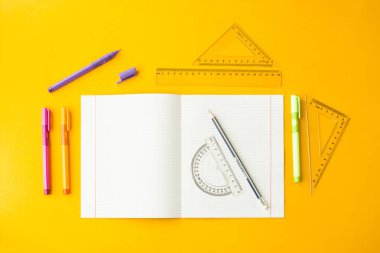 Defter kalem, kurşun kalem ve sarı bir arka plan üzerindeki cetvellere arasında bir hücrede. Çalışma için aksesuarlar. Matematik. Üstten görünüm, düz yatıyordu