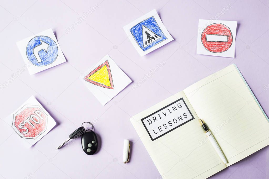 Training notebook for driving lessons and driving traffic rules next to the road sign drawings to get a driving license. On a purple background next to the car keys