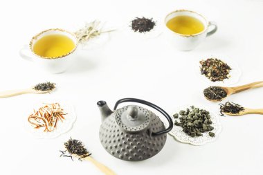 Gri demir su ısıtıcısı bir daire ve bardak beyaz bir masada hazır bir içkiyle dizilmiş kuru çay çeşitleri arasında