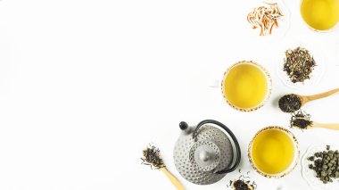 Gri demir tencere çeşitleri kuru çay ve su bardağı beyaz bir masada hazır bir içkiyle arasında. Üstten görünüm, düz yatıyordu. Kopya alanı