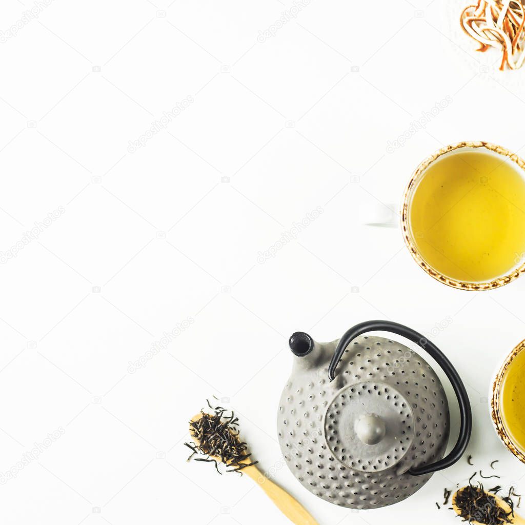Gray iron kettle among different kinds of dry tea and cups with a ready drink on a white table. Top view, flat lay. Copy space