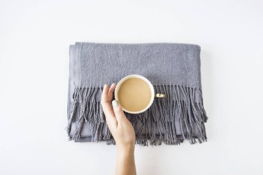 Gri kaşmir kadın eşarp bir dikdörtgen beyaz bir arka plan üzerinde katlanmış. Bir kadının el ve bir fincan sütlü kahve ile. Minimalizm. Üstten görünüm, düz yatıyordu