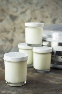 Dört yanındaki gri bir arka plan üzerine yoğurt makinesi ev yapımı yoğurt ile kavanozları. Diyet gıda