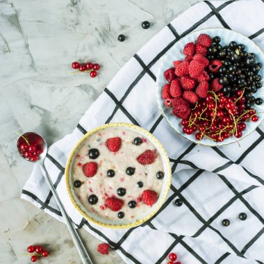 Bir tabak bir tabak kırmızı ve siyah kuş üzümü ve ahududu yanındaki damalı beyaz peçeteye çilek ile yulaf ezmesi. Sağlıklı gıda kavramı