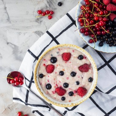 Bir tabak bir tabak kırmızı ve siyah kuş üzümü ve ahududu yanındaki damalı beyaz peçeteye çilek ile yulaf ezmesi. Sağlıklı gıda kavramı