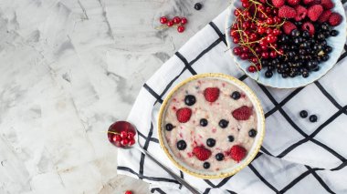 Bir tabak bir tabak kırmızı ve siyah kuş üzümü ve ahududu yanındaki damalı beyaz peçeteye çilek ile yulaf ezmesi. Sağlıklı gıda kavramı