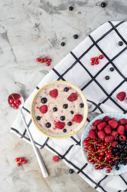 Bir tabak bir tabak kırmızı ve siyah kuş üzümü ve ahududu yanındaki damalı beyaz peçeteye çilek ile yulaf ezmesi. Sağlıklı gıda kavramı