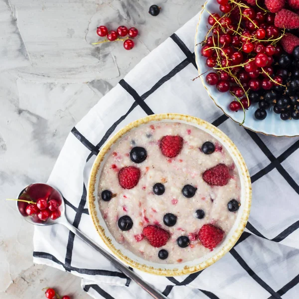 Bir tabak bir tabak kırmızı ve siyah kuş üzümü ve ahududu yanındaki damalı beyaz peçeteye çilek ile yulaf ezmesi. Sağlıklı gıda kavramı