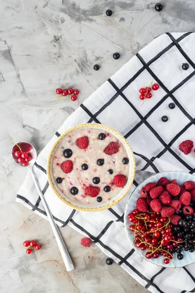 Bir tabak bir tabak kırmızı ve siyah kuş üzümü ve ahududu yanındaki damalı beyaz peçeteye çilek ile yulaf ezmesi. Sağlıklı gıda kavramı