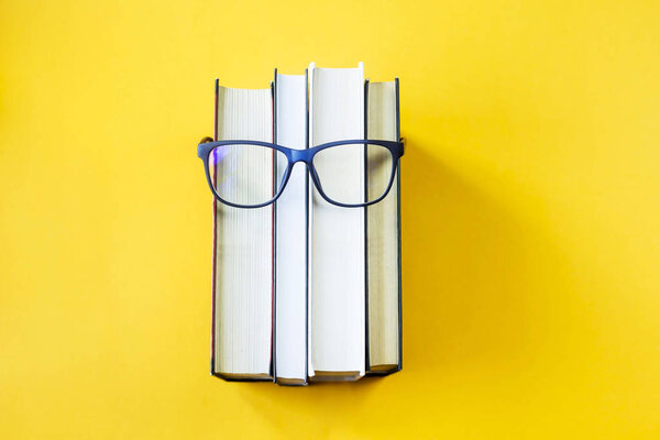 Куча книг в очках - это изображение лица человека. Концепция чтения и обучения. На ярко-желтом фоне
