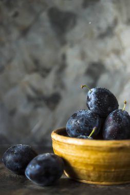 Olgun mavi Erik bir kil kase gri bir tablo. Yaz mevsim meyveleri kavramı