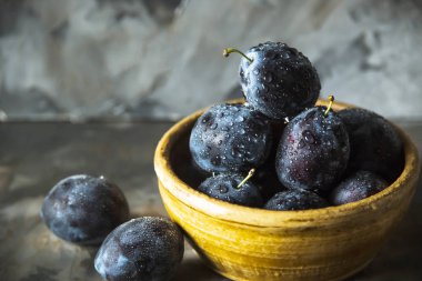 Olgun mavi Erik bir kil kase gri bir tablo. Yaz mevsim meyveleri kavramı