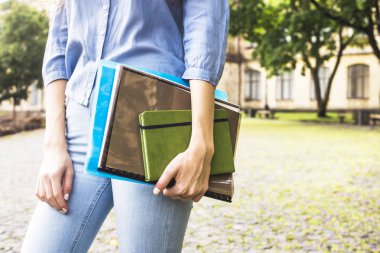 Uzun kıvırcık saçlı bir kız öğrencinin eğitim materyalleri üniversite avlusunda klasörlerde tutuyor. Yüksek öğretim kavramı