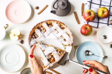 Ev yapımı elma pasta bir parça kadın elinde bir tepside pudra şekeri serpilir. Bardaklar, tabaklar, elma, tarçın ve anason arasında bir aile tablosu arka planı. Pişirme sonbahar