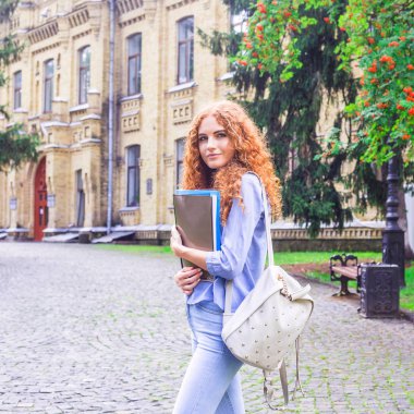 Kızıl saçlı kız öğrenci klasörleri ve öğretim materyalleri üniversitenin yanında elinde. Geri okul kavramı. öğrenci yaşamı