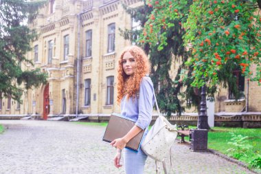 Kızıl saçlı kız öğrenci klasörleri ve öğretim materyalleri üniversitenin yanında elinde. Geri okul kavramı. öğrenci yaşamı