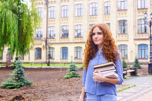 Kızıl saçlı kız öğrenci ile bir yığın kitap Üniversitesi Kitaplığı'ndan geliyor. Eğitim ve yüksek öğretim kavramı