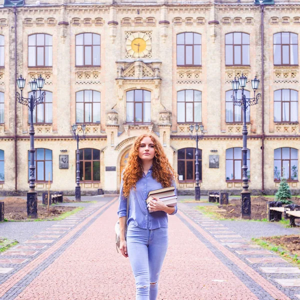 Kızıl saçlı kız öğrenci ile bir yığın kitap Üniversitesi Kitaplığı'ndan geliyor. Eğitim ve yüksek öğretim kavramı