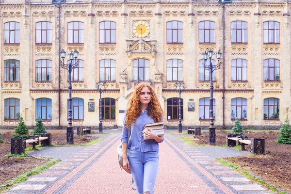 Kızıl saçlı kız öğrenci ile bir yığın kitap Üniversitesi Kitaplığı'ndan geliyor. Eğitim ve yüksek öğretim kavramı