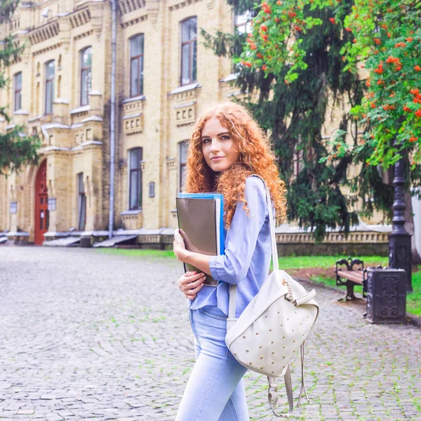 Kızıl saçlı kız öğrenci klasörleri ve öğretim materyalleri üniversitenin yanında elinde. Geri okul kavramı. öğrenci yaşamı