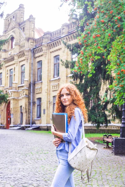 Kızıl saçlı kız öğrenci klasörleri ve öğretim materyalleri üniversitenin yanında elinde. Geri okul kavramı. öğrenci yaşamı