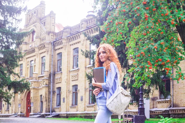 Kızıl saçlı kız öğrenci klasörleri ve öğretim materyalleri üniversitenin yanında elinde. Geri okul kavramı. öğrenci yaşamı