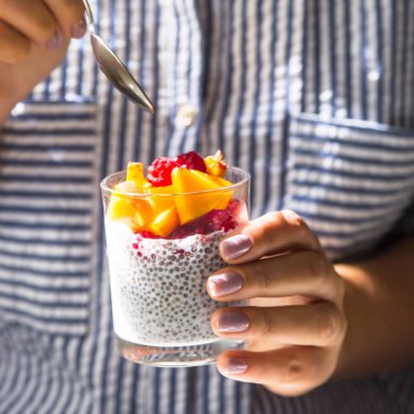 Hindistan cevizi sütü ile ahududu ve kadın elinde bir kaşık ile cam kavanozda şeftali üzerinde Chia puding. Çiğ vegan sağlıklı gıda kavramı