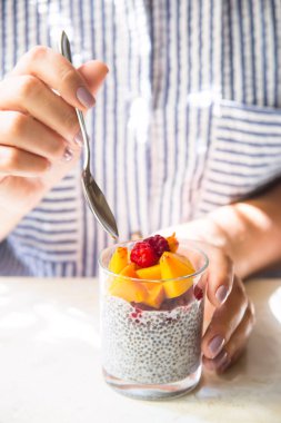 Hindistan cevizi sütü ile ahududu ve kadın elinde bir kaşık ile cam kavanozda şeftali üzerinde Chia puding. Çiğ vegan sağlıklı gıda kavramı