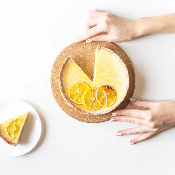 Lemon tart with dried lemons as a decoration and a cut piece in female hands. On a white background. Top view, flat lay. Homemade minimal backing