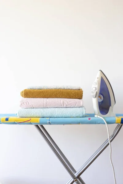 Home ironing of towels on the ironing board. Iron next to a pile of clean fresh towels Homework concept