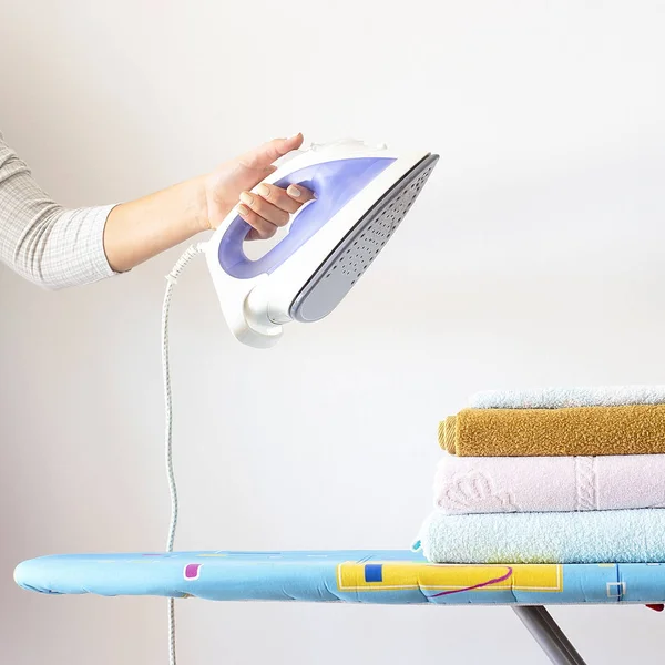 A woman\'s hand holds an iron over a pile of clean ironed towels on the ironing board. Homework Concept