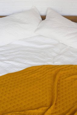 Beyaz yastıklar, bir sayfa ve bir battaniye ile sarı sıcak bir battaniye ile bir yatak. Ev minimalist iç ve rahatlık