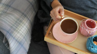 Kadın elleriyle pembe ve turkuaz şamdanlar ile damalı toz halı gri rahat kanepe üzerinde bir ahşap tepsi sütlü kahve bir fincan. İç ve ev rahatlık kavramı. Üstten görünüm