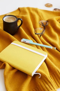 Not defteri, kalem, bardak ve bir fincan kahve ile sarı parlak kazak. Sonbahar ruh hali ve stil. Üstten görünüm, düz yatıyordu