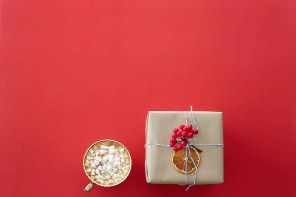 赤い背景の上にマシュマロとココアのカップでガマズミの赤い小枝で飾られたペーパー クラフトのクリスマス ギフトが満載です コピー スペース平面図 — ストック写真