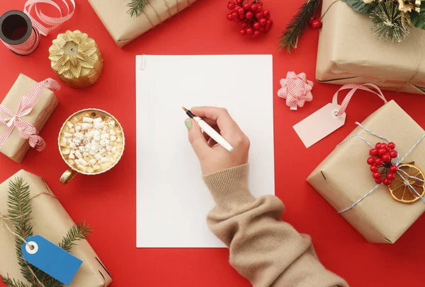 Mâna Feminină Scrie Foaie Albă Hârtie Printre Cadourile Crăciun Decorațiuni — Fotografie, imagine de stoc