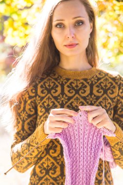 Kahverengi bir süveter gülümseyen ve mor örgü fular örgü iğne tutarak uzun saçlı beyaz kız. Sonbahar sıcak el yapımı giyim