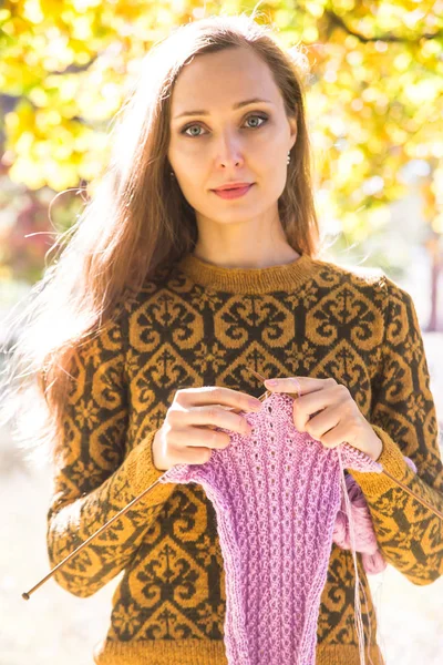 长头发的白种女孩 穿着棕色毛衣 微笑着用一条紫色针织围巾握住针织针 秋暖手做的衣服 — 图库照片