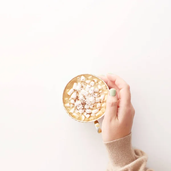 A cup of cocoa with marshmallows on a white background in a female hand. Winter days concept. Minimalism. Top view, flat lay