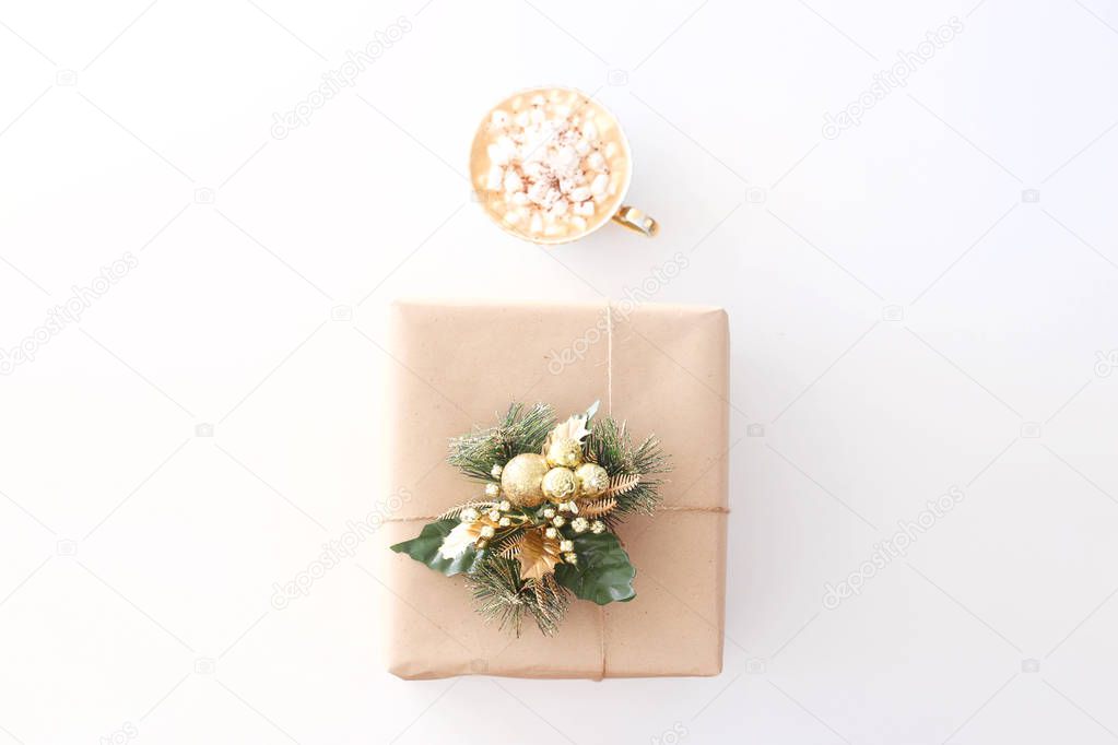 Christmas New Year's gift in craft paper decorated with a spruce branch next to a cup of cocoa with marshmallow on a white background. Top view, flat lay