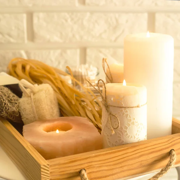 Ecological accessories for a spa in a home bathroom on a wooden tray with candles against a white brick wall