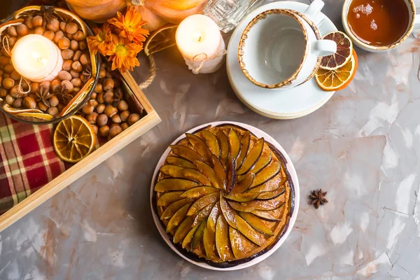 Plum cake decorated with sliced plum among the autumn decor - pumpkin, candle, oranges and yellow chrysanthemum. Rustic style. Homely cozy flat lay. Top view