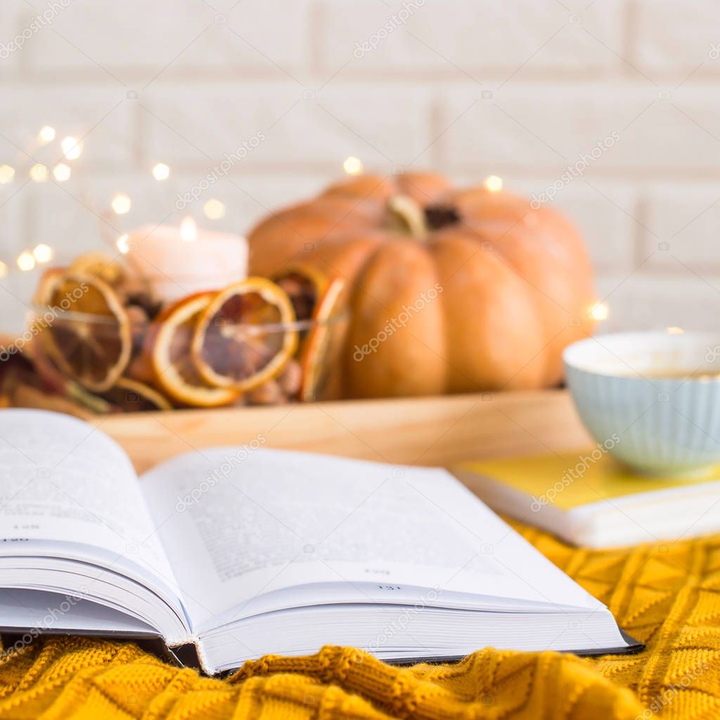 Homely cozy rest on an autumn day off - reading among blankets with a cup of coffee next to candles, dried oranges and pumpkin